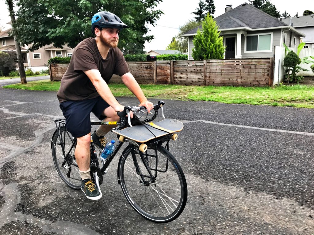 Carl Harling riding his bike with his board strapped to the basket on a mission for mental health in memory of Ben Raemers
